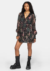 A model wearing a black and pink floral long-sleeve mini dress with a tie-neck and cinched waist, paired with chunky black combat boots, against a light gray studio background.