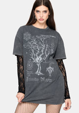 A woman modeling a dark gray acid-wash t-shirt with a white gothic tree and occult graphic print, layered over a black lace long-sleeve top and fishnet tights against a light gray studio background.
